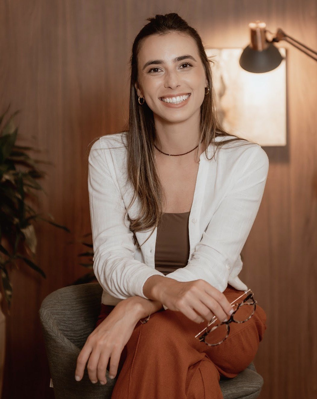 Laís Cohn sorrindo, sentada com os óculos na mão